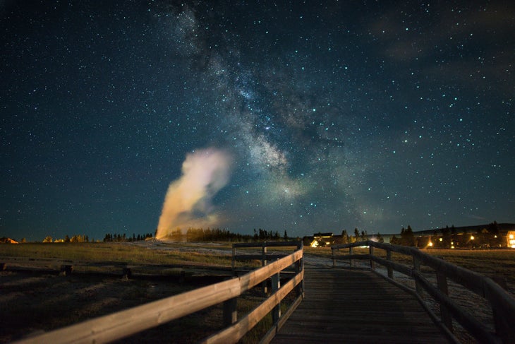 Old Faithful Geyser erupts under the Milky Way from the boardwalks in the Upper Geyser Basin