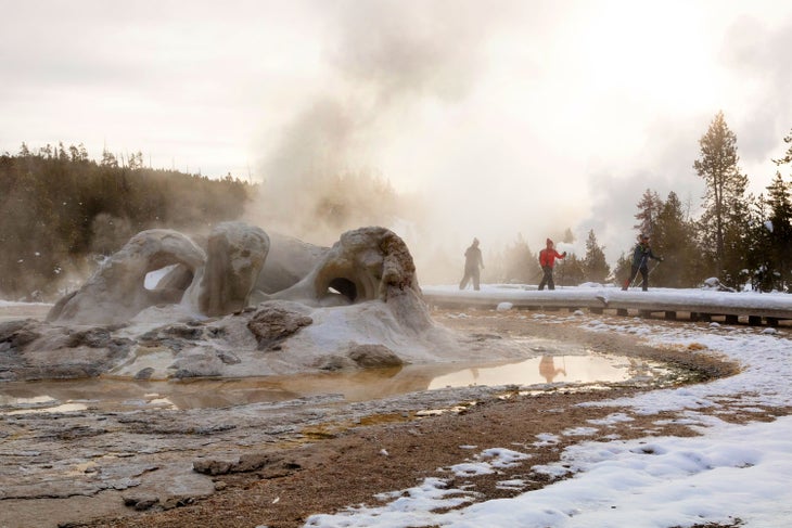Skiers on the boardwalks near a steamy Grotto Geyser